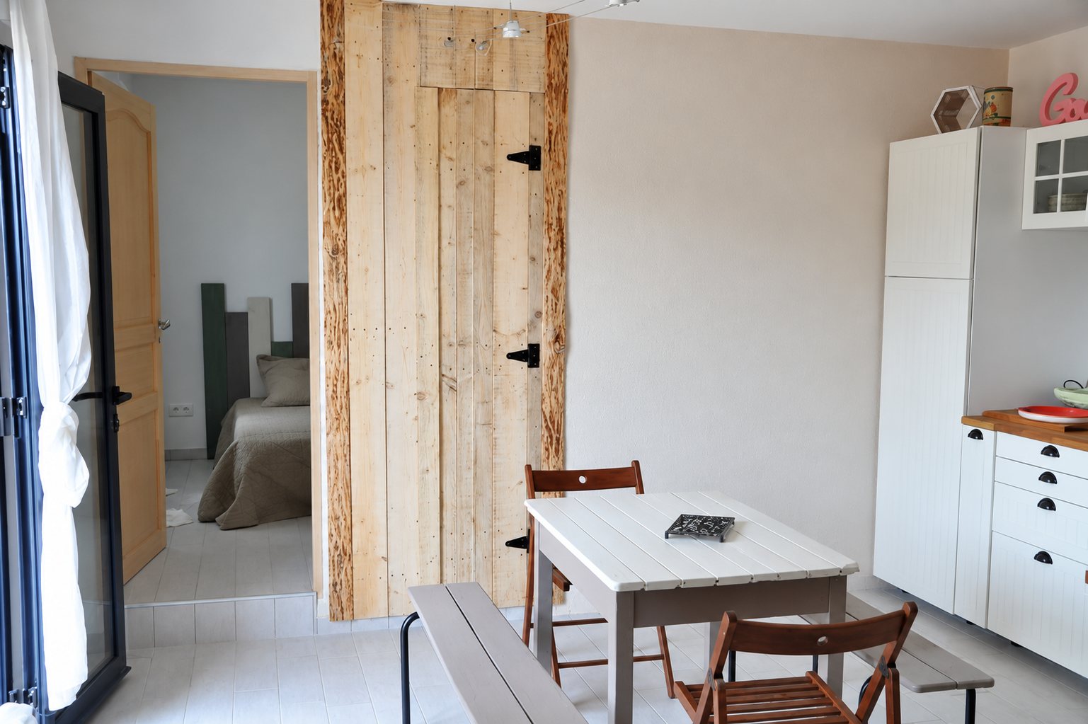 Pièce à vivre avec table blanche, porte en bois brut et chambre au fond